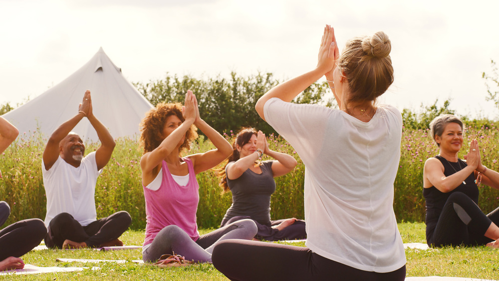 Female Teacher Leading Group Of Mature Men And Women In Class At Outdoor Yoga Retreat